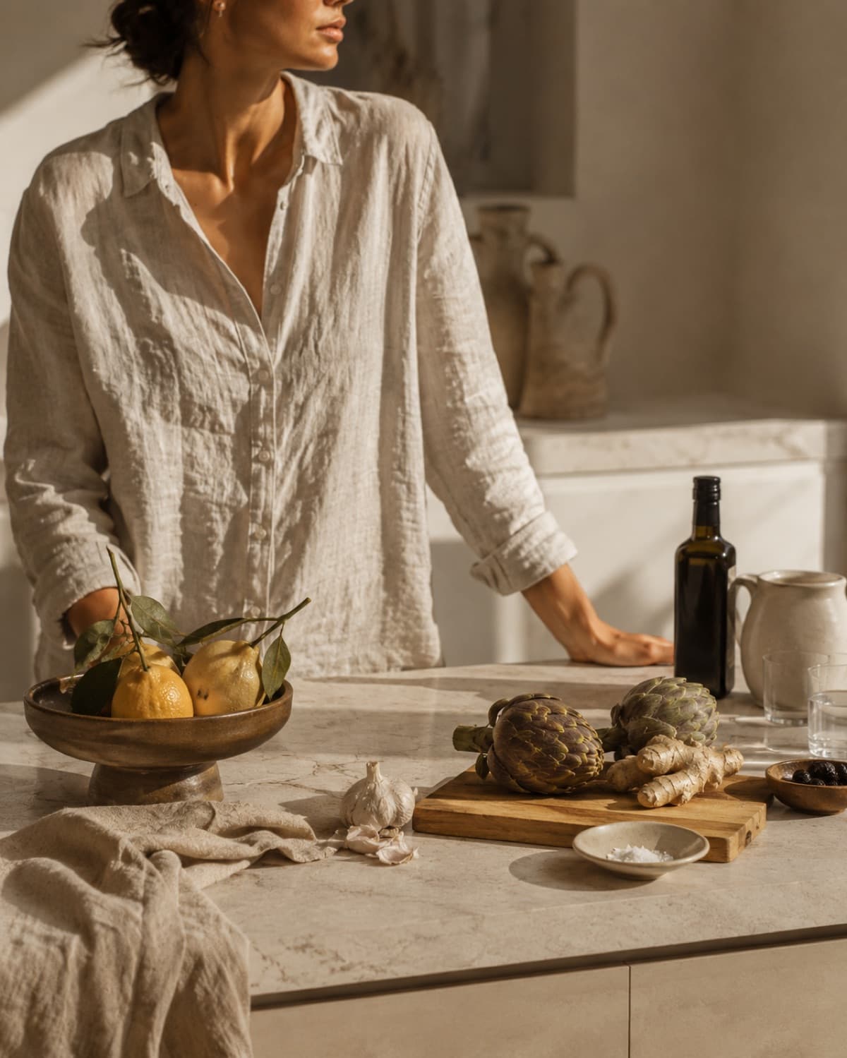 Plan de travail en pierre claire, citrons, artichauts et huile d'olive dans la lumière de fin de journée